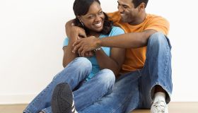 Happy, smiling African American couple sitting on floor snuggling.