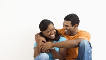 Happy, smiling African American couple sitting on floor snuggling.