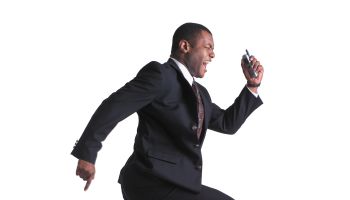 an african american business man holds a cell phone and leaps through the air