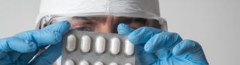 A scientist examines a pack of pills of vaccine against the Omicron mutation of COVID-19 and other mutations. He is wearing a protective mask, glasses and a protective suit.