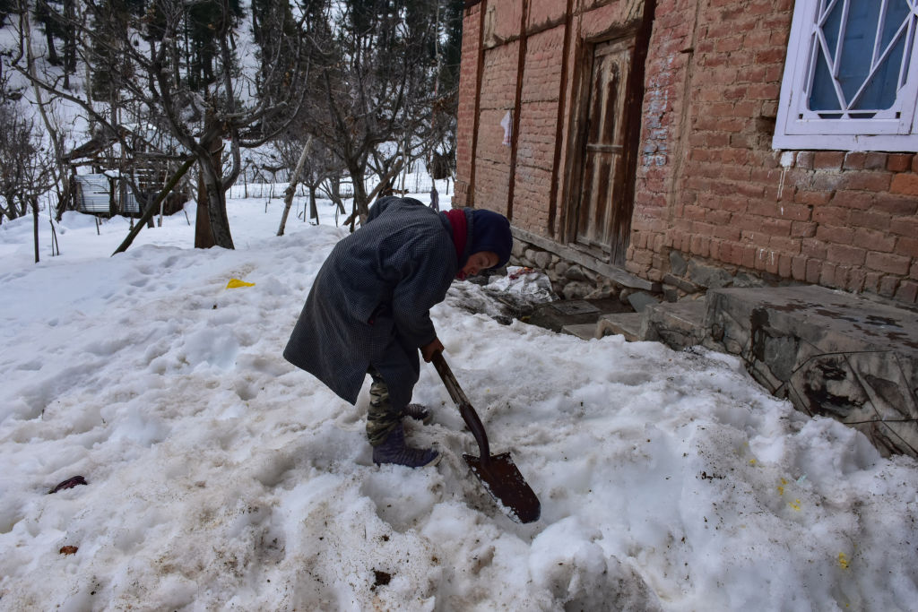 A boy clears snow outside his house during a sunny winter...