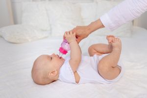a 6-month-old baby lies on a white bed and drinks milk from a bottle, baby food concept, text space