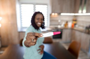Smiling beautiful black woman showing positive pregnancy test