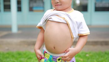 Close up happy little boy lifting his shirt show exposing his big tummy.