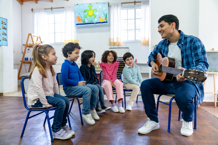 Diverse group of 7 year olds at school having fun in music class with male cheerful teacher