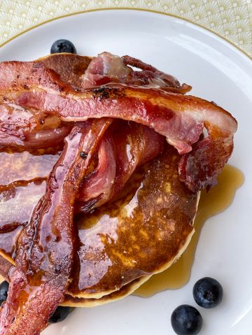 Full frame image of fresh stack of fluffy, American-style pancakes, grilled bacon rashers and blueberries drizzled with dripping maple syrup on plate, elevated view