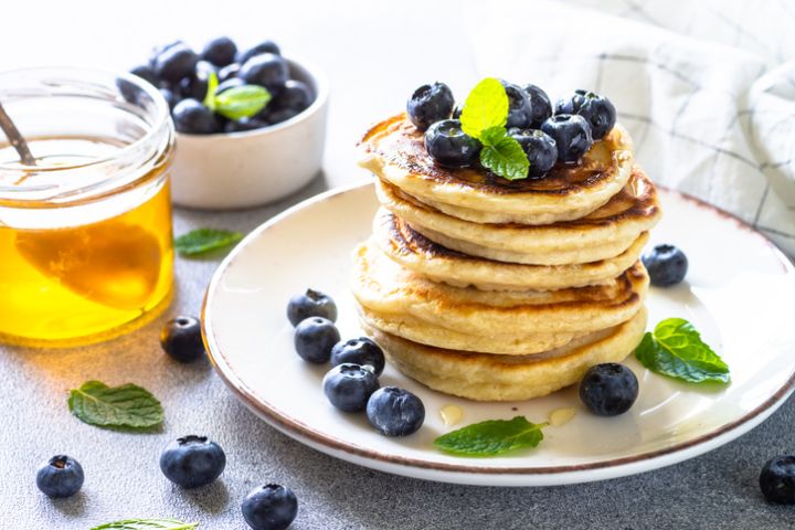 Pancakes with fresh blueberries and honey at white table.
