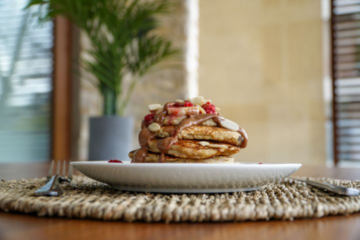 Plate of oatmeal and banana pancakes with raspberries and peanut butter served on a wooden table with decorative plants. Vegan dish, healthy and delicious.