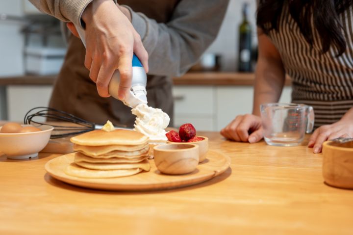 A man spraying whipped cream on pancakes while enjoying cooking with his girlfriend