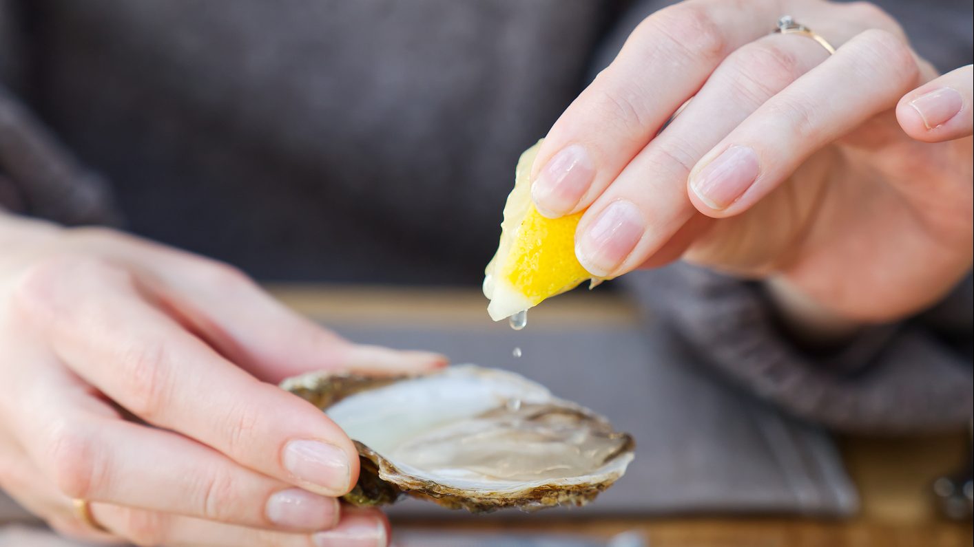 Beautiful Woman eating fresh oysters and drinking in restaurant. Seafood delicacies.
