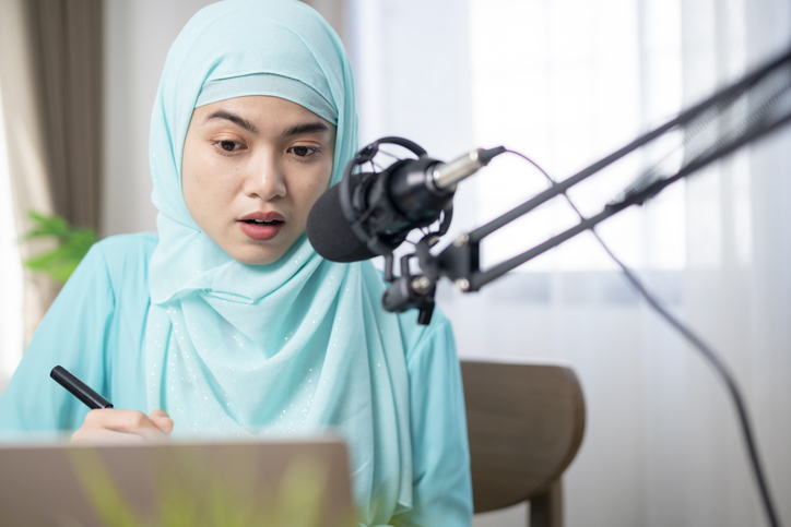 Muslim woman wearing hijab and headphones listening to audiobooks and podcasts at home, satisfied and successful woman.
