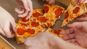 Home party. Top view male female hands taking slices of pizza from food delivery open box. Group of hungry friends sharing delicious lunch eating ordered pepperoni pizza. Food pizza delivery.