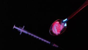 Syringes and heroin powder on black background with red blue neon light. Addict concept