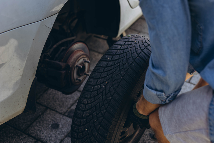 Young man in unscrewing lug nuts on car wheel in process of new tire replacement,using wrench while changing flat tire on the road.