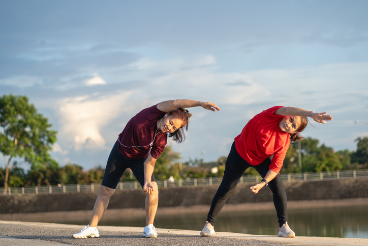 Two healthy senior women enjoy exercising on a walkway by a pond in a park.