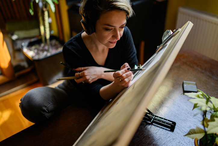 Skilled illustrator pencil drawing and listening music on headphones.