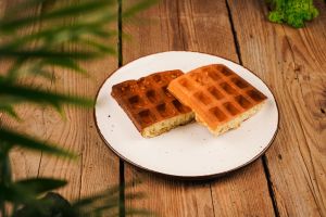 Waffles on plate isolated on dark background. Delicious Belgian waffles on wooden table. Burnt Belgian waffles. Belgian waffles on a white plate, front view. Homemade simple pastries.