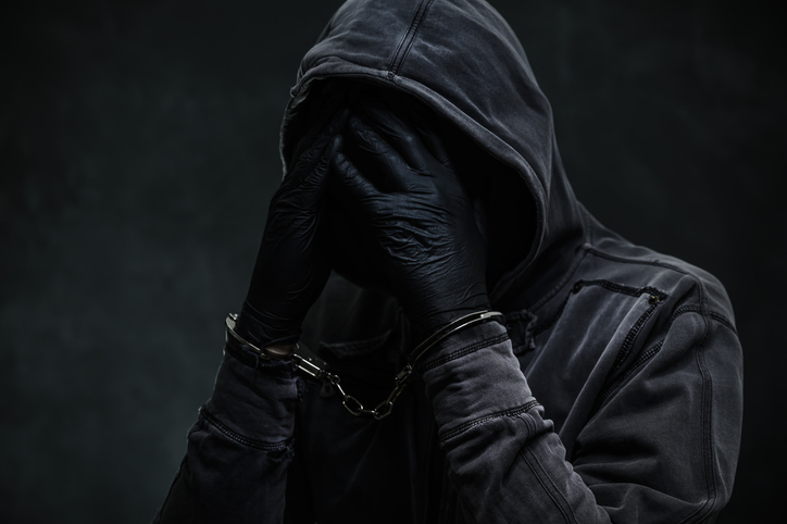 Handcuffed criminal wearing hoodie and covering face with hands