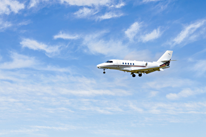 Private business plane flying under a blue sky with white clouds