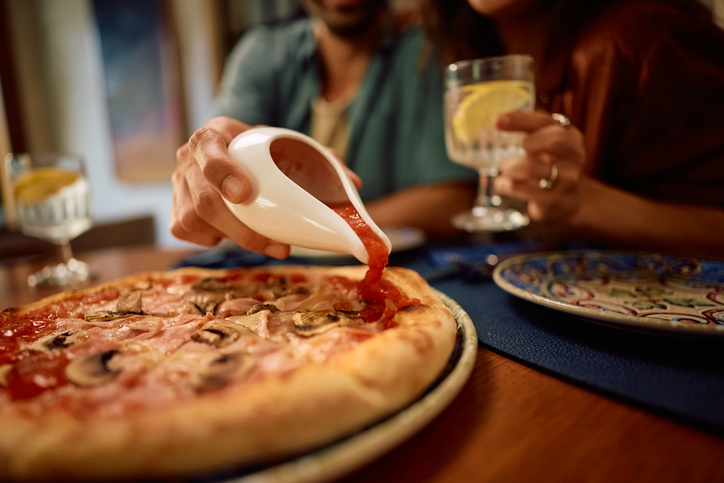 Close up of man pouring ketchup on a pizza.