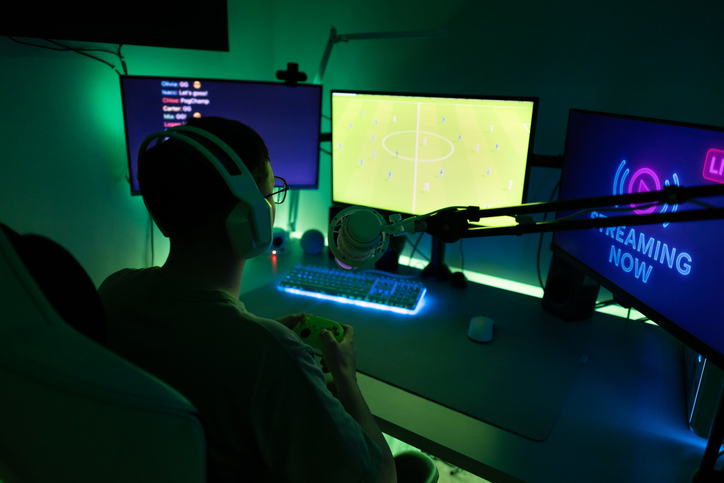 Gamer playing joystick controller in a dark room with green and blue neon lights, streaming live video games online