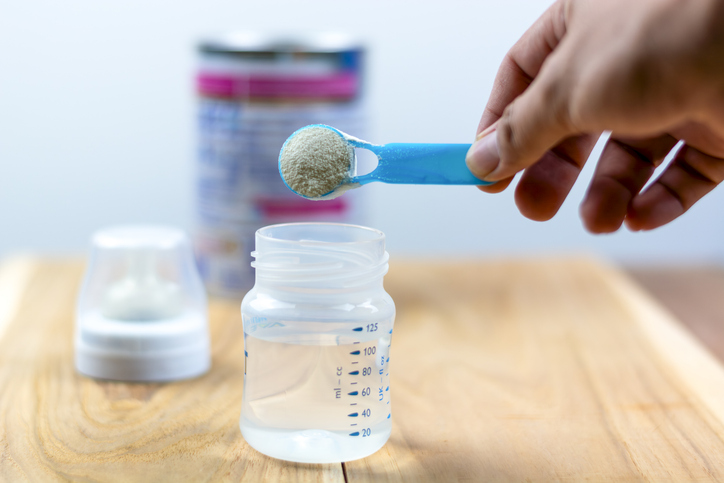 Powder milk and blue spoon on light background close-up. Milk powder for baby in measuring spoon on can. Powdered milk with spoon for baby. Baby Milk Formula and Baby Bottles
