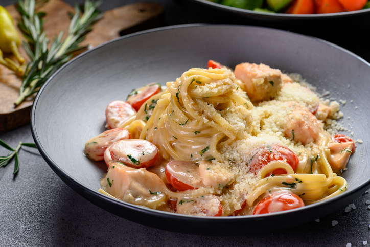 Delicious pasta dish with tomatoes and herbs served in a bowl. A bowl holds cooked pasta mixed with tomatoes and herbs. The dish is ready to eat.