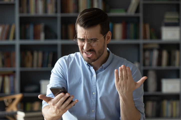 Nervous angry young businessman reading rejection notice on smartphone screen