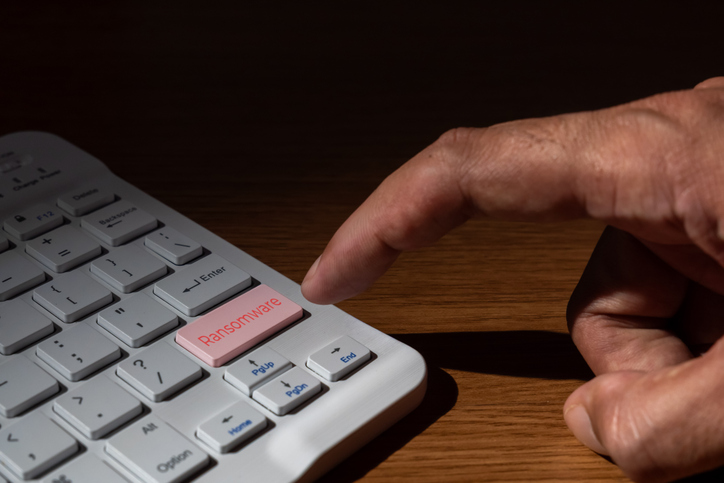 Close-up of a finger pressing a Ransomware key on a white computer keyboard.