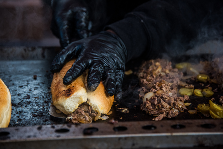 Vendor Assembling Philly Cheesesteak On Charcoal Grill At Broadway