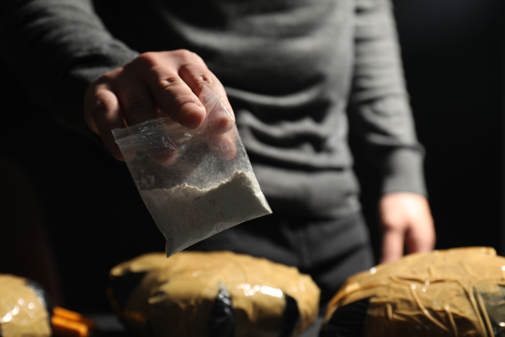 Smuggling and drug trafficking. Man holding plastic bag with cocaine on dark background, closeup