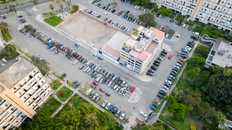 Drone view of urban parking area and surrounding buildings.