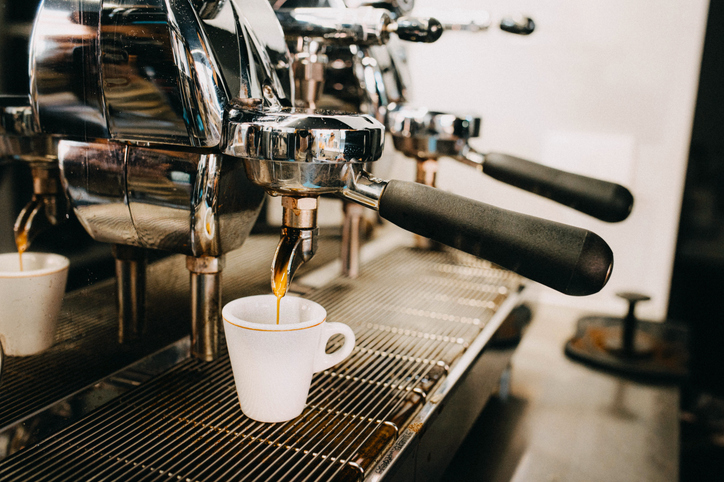 A professional espresso machine with shiny chrome details is seen brewing coffee into a ceramic cup