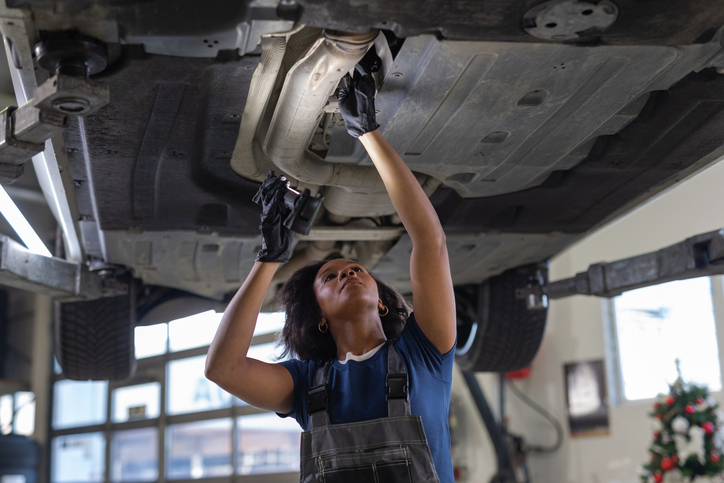 African American female mechanic with a flashlight inspecting the car underside