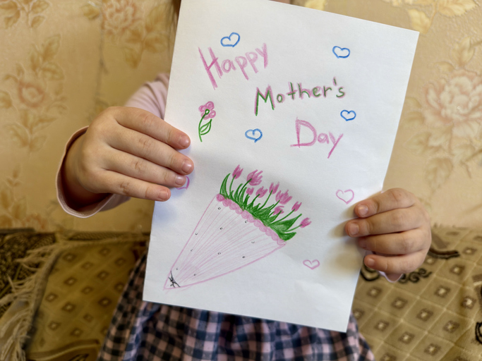 Child holding a handmade greeting card for Mother's Day