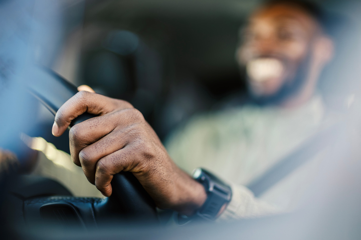 Hand gripping steering wheel while man driving car