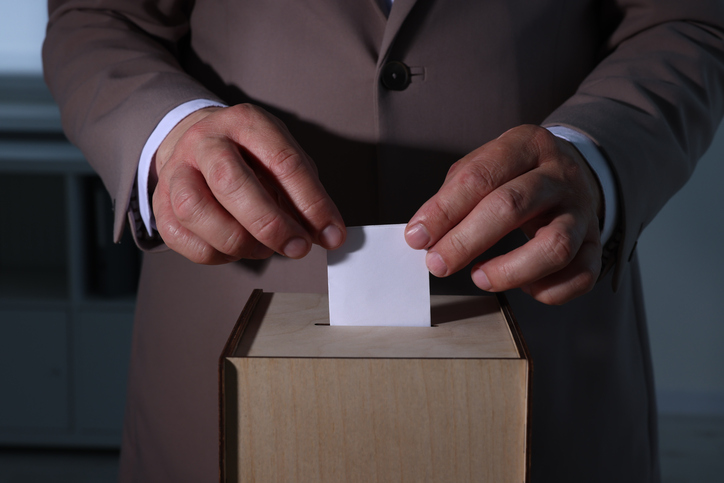Man putting his vote into ballot box indoors, closeup
