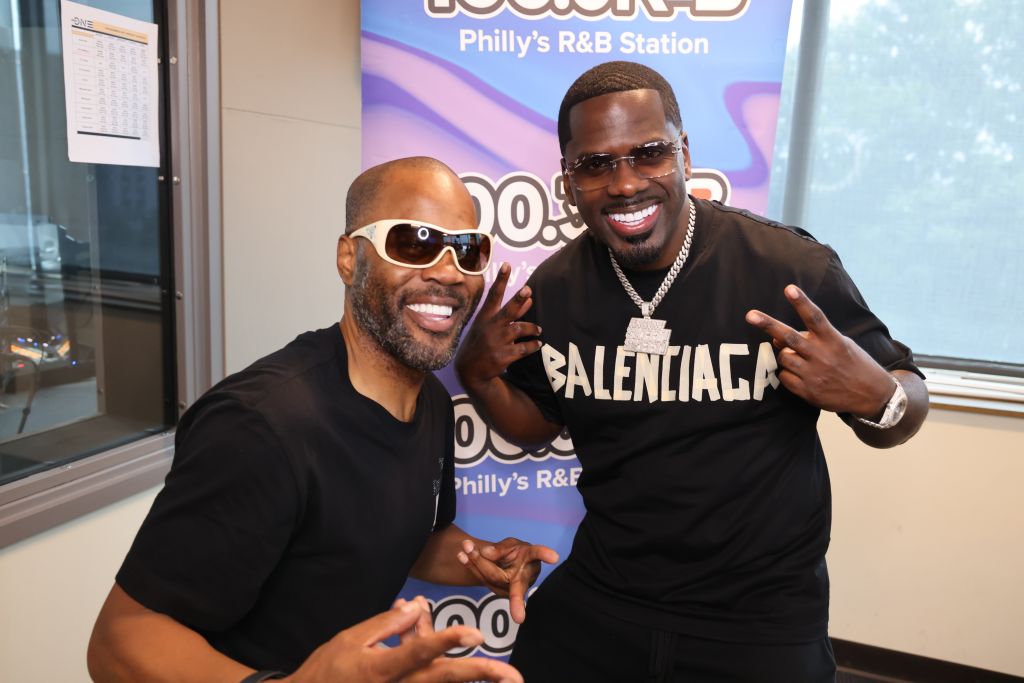 Two men wearing sunglasses and Balenciaga clothing posing together in front of a sign for "Philly's R&B Station".