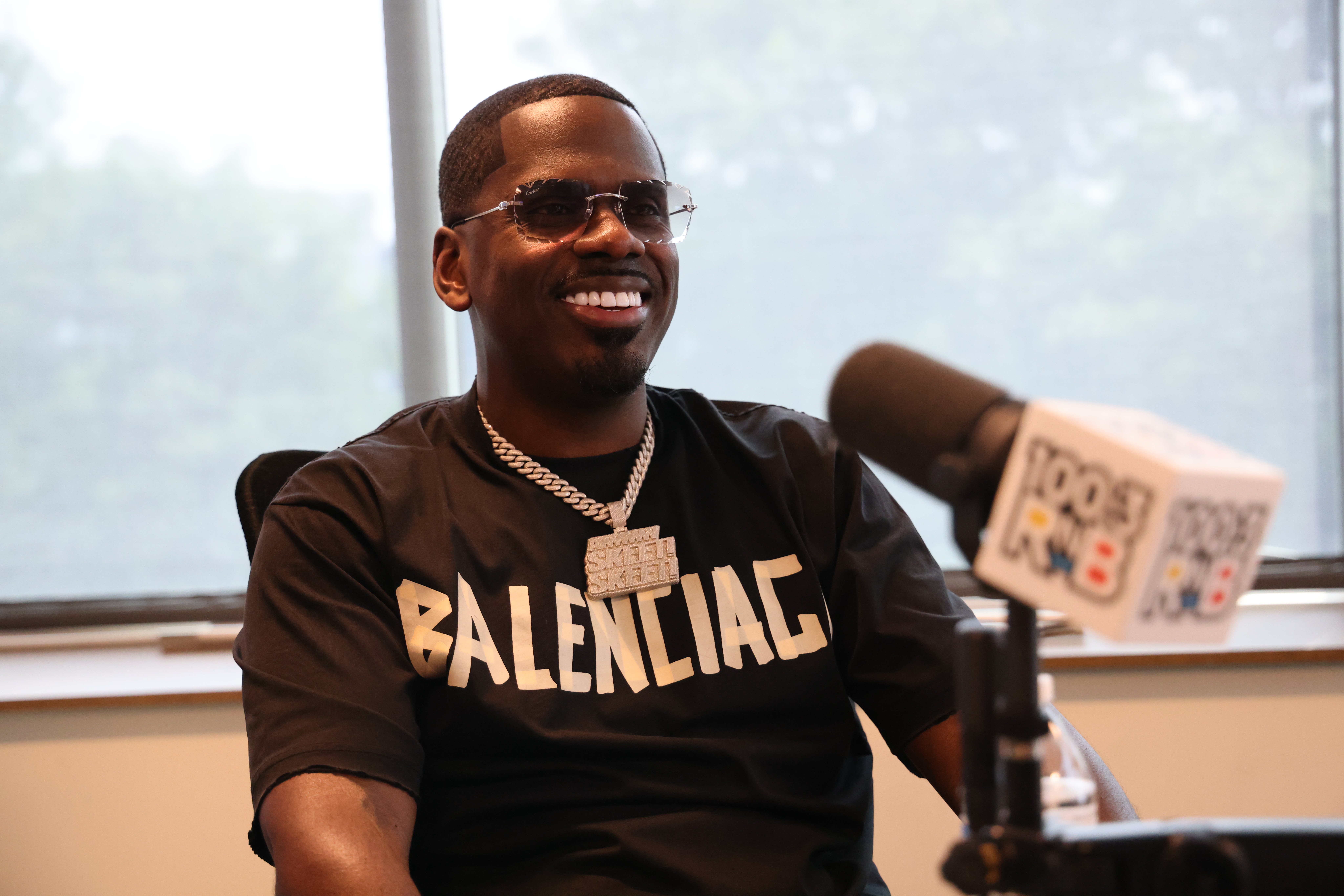A smiling man wearing a black t-shirt with the text "BALENCIAG" printed on it.