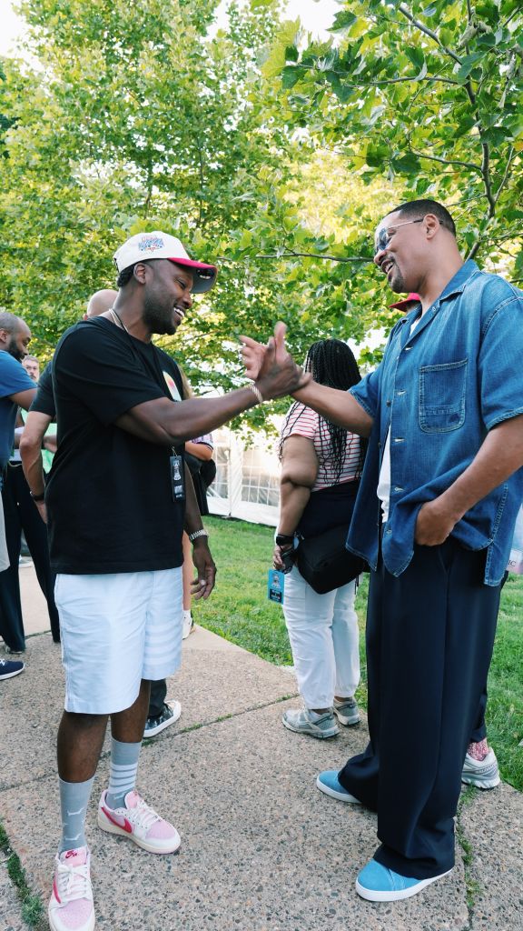 Two men standing in a park, engaged in a friendly conversation and gesturing with their hands.