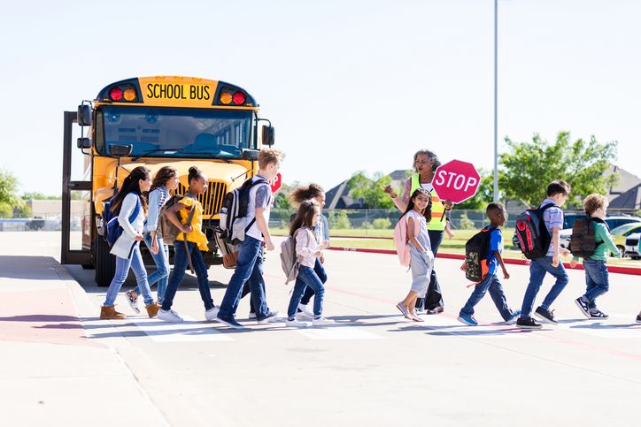 Students cross the street safely with crossing guard near yellow school bus