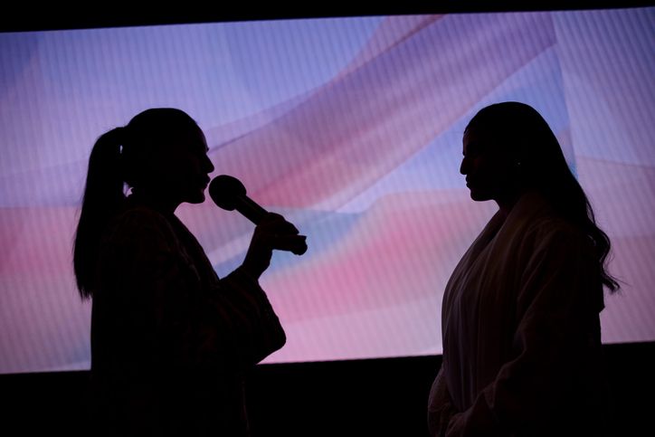 Conducting an interview on a stage. Two women are on stage, with one silhouetted as she interviews the other.