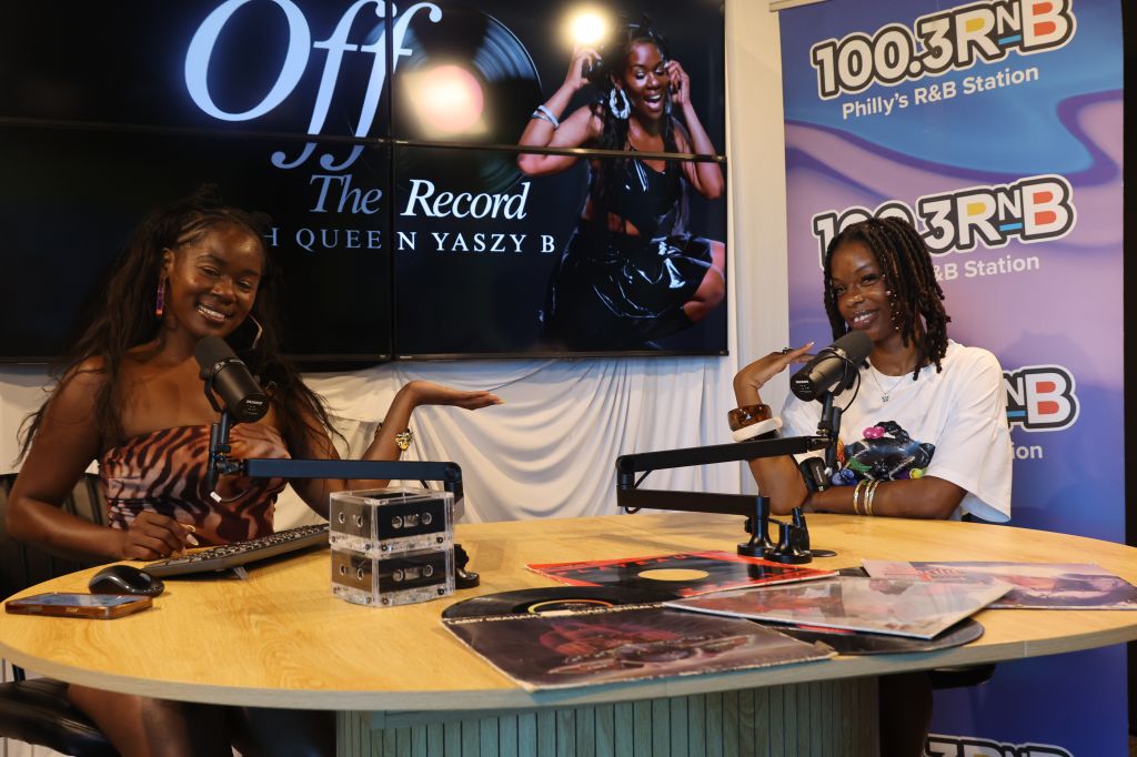 Two women sitting at a radio station desk, smiling and speaking into microphones. The backdrop features the "Off the Record" logo and "100.3 RNB" station branding.