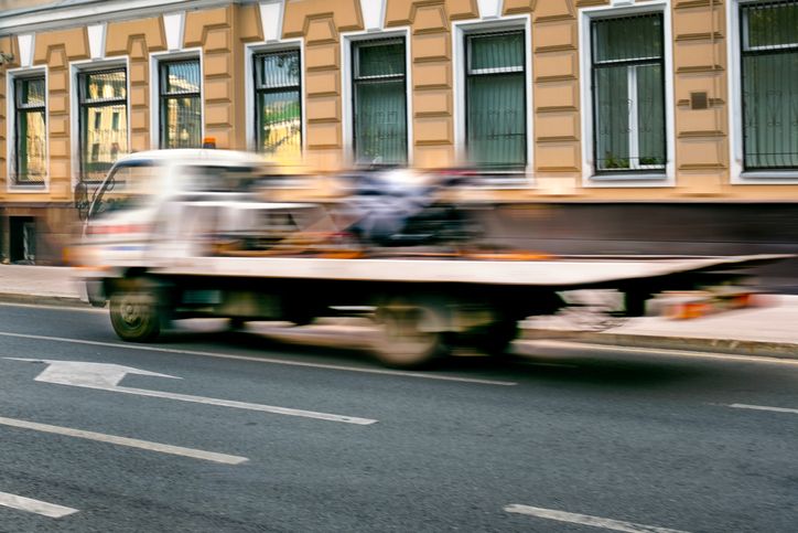 Tow truck with full platform moves along a city street