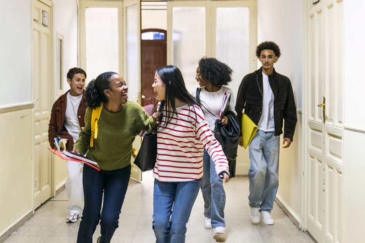 Diverse students laughing walking along school hallway