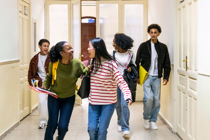 Diverse students laughing walking along school hallway